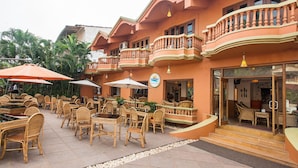 An outdoor seating area with wicker furniture and umbrellas, a sign for 'ruffles', and a building with balconies. - Ruffles Beach Resort (Candolim)