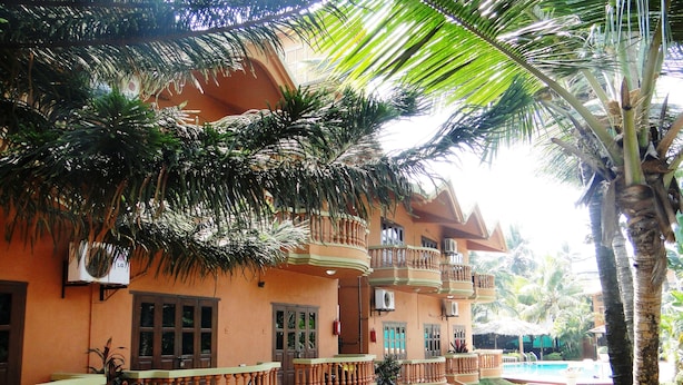 A multi-story building with balconies, a swimming pool, and lush greenery. - Ruffles Beach Resort (Candolim)