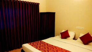 A hotel room with a bed, pillows, a red and white bedspread, a dark-colored wardrobe, and a curtain. - Ruffles Beach Resort (Candolim)