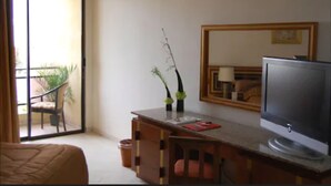 A hotel room with a sliding glass door to a balcony, a wooden desk with a television, and a chair. - Hotel Diplomat (Tunis)