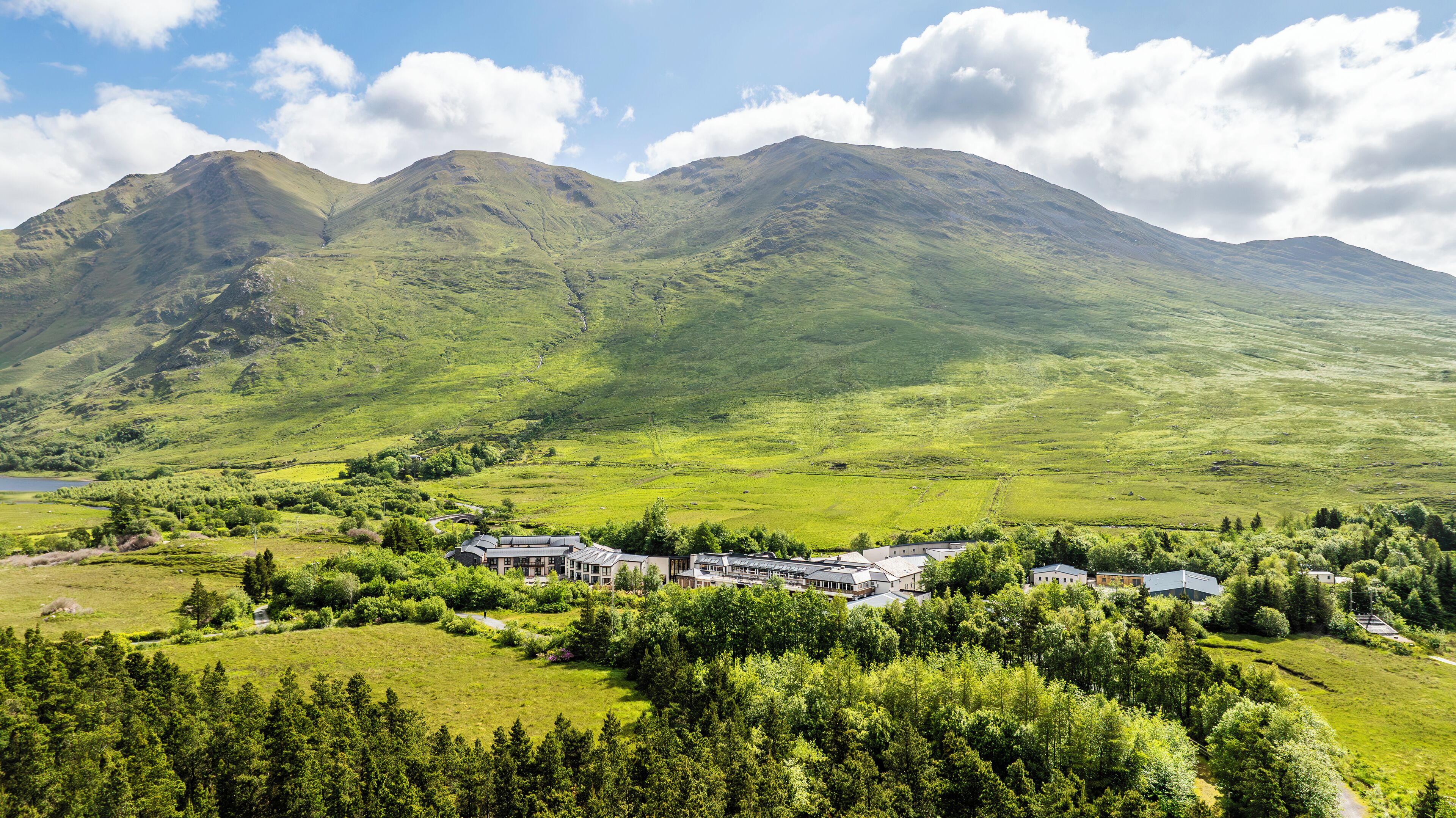 A hotel with multiple buildings, surrounded by lush green fields and mountains in the background.