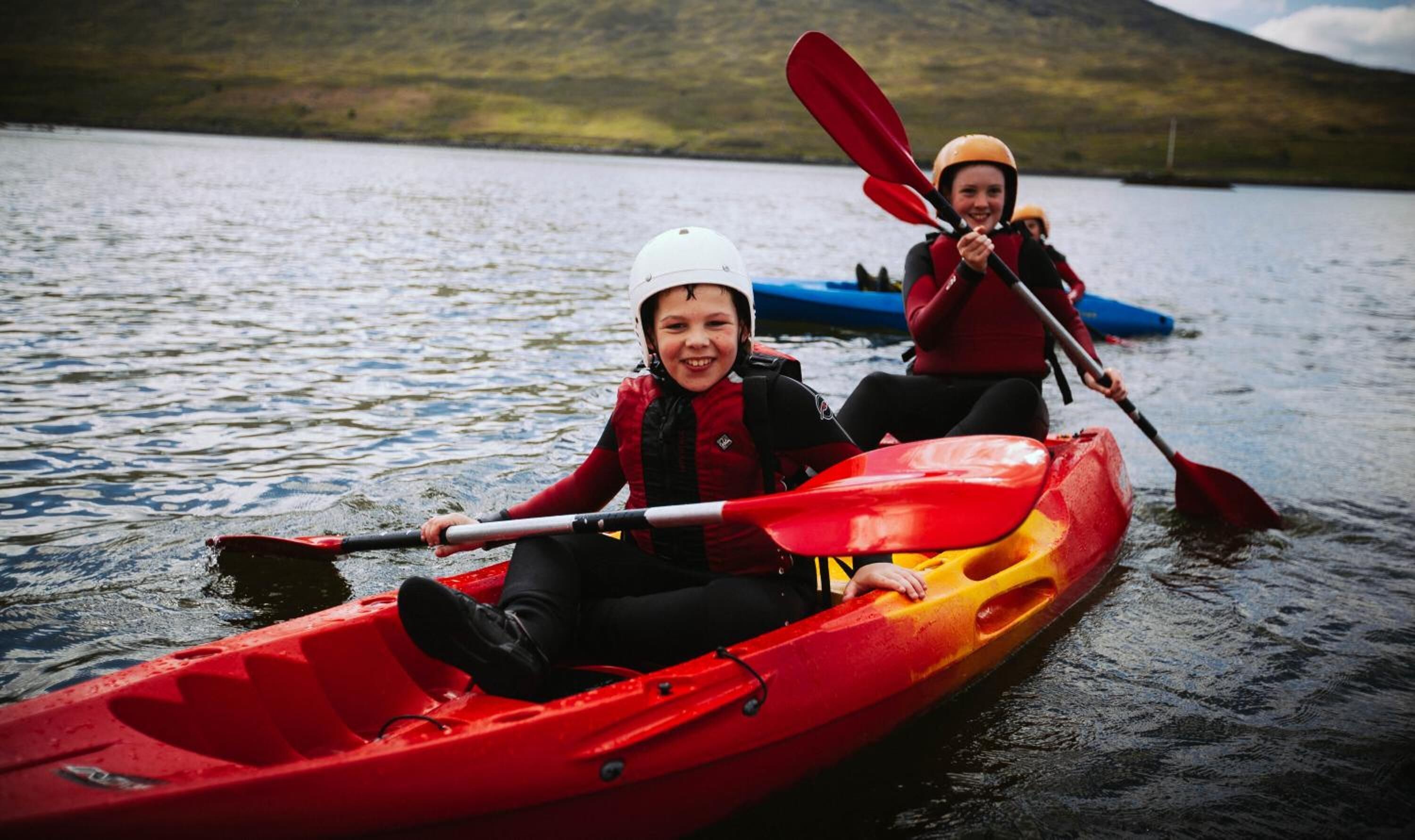 Dues persones fent kayak en un llac tranquil amb un paisatge amb turons al fons.
