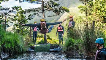 Un grupo de personas con equipo de senderismo junto a un río, con árboles y montañas al fondo.
