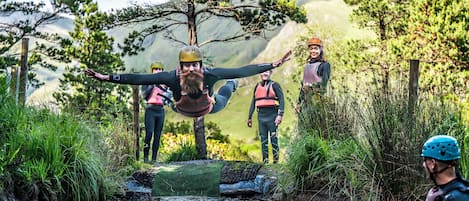 A group of people in outdoor gear by a river, with trees and mountains in the background.
