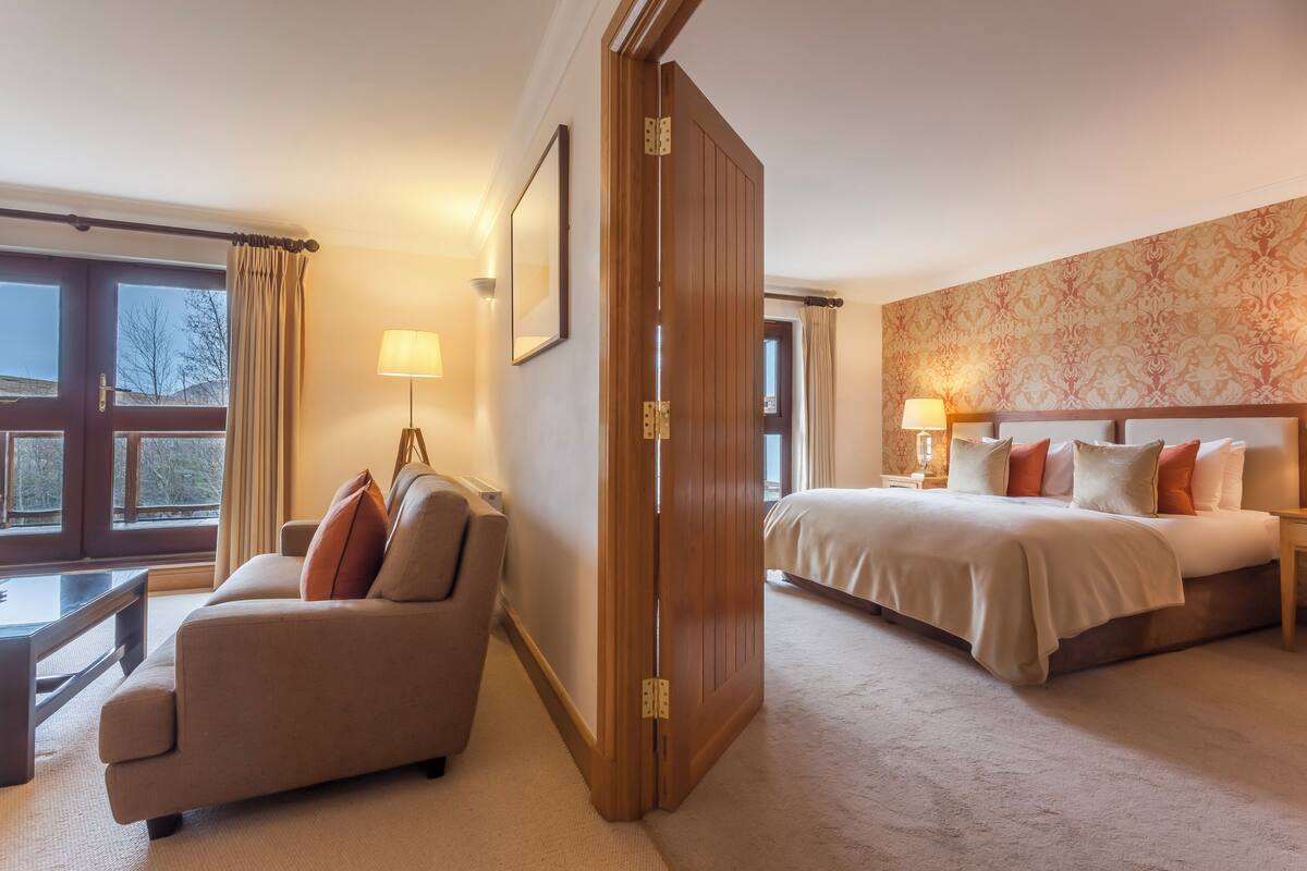 A hotel room with a sofa, a bed, a desk, and a large window with curtains.