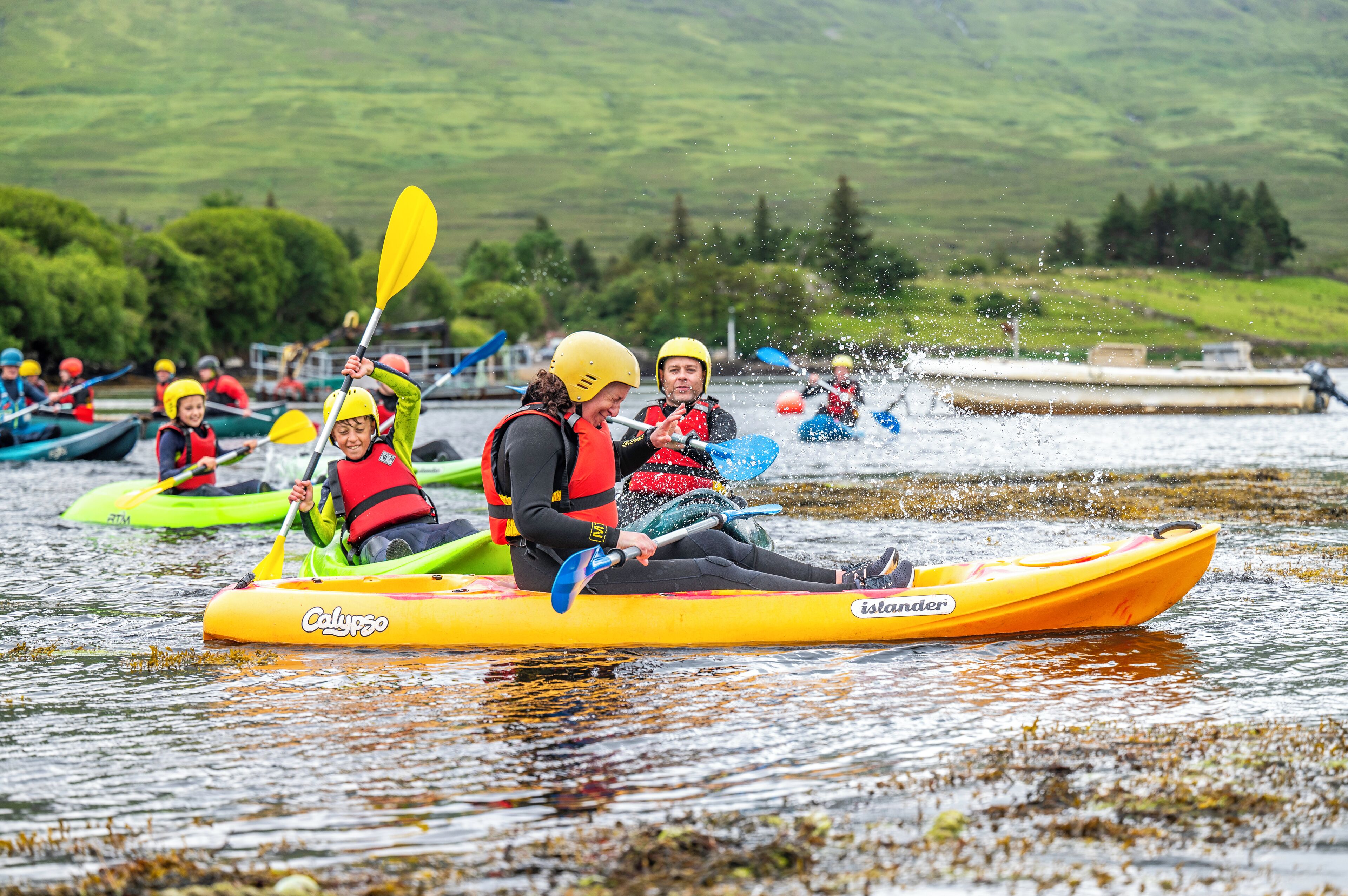 Un groupe de personnes pratiquant le kayak sur un lac, avec un paysage verdoyant et pittoresque en arrière-plan.