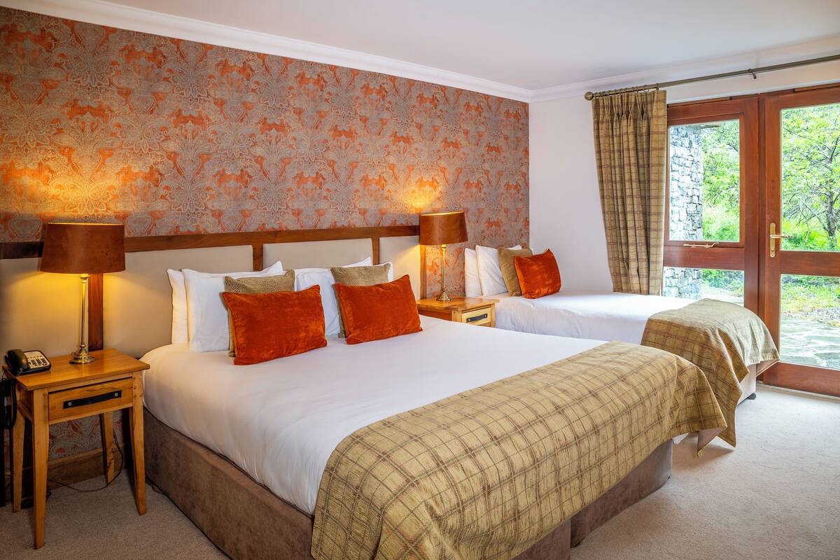 A hotel room with two beds, a patterned wall, and a view through a glass door.