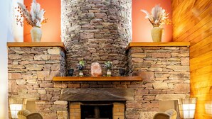 A cozy interior with a stone fireplace, two armchairs, and a wooden ceiling. - Delphi Resort (Leenane)
