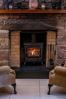 Una chimenea de piedra con estufa de leña, flanqueada por dos sillones.