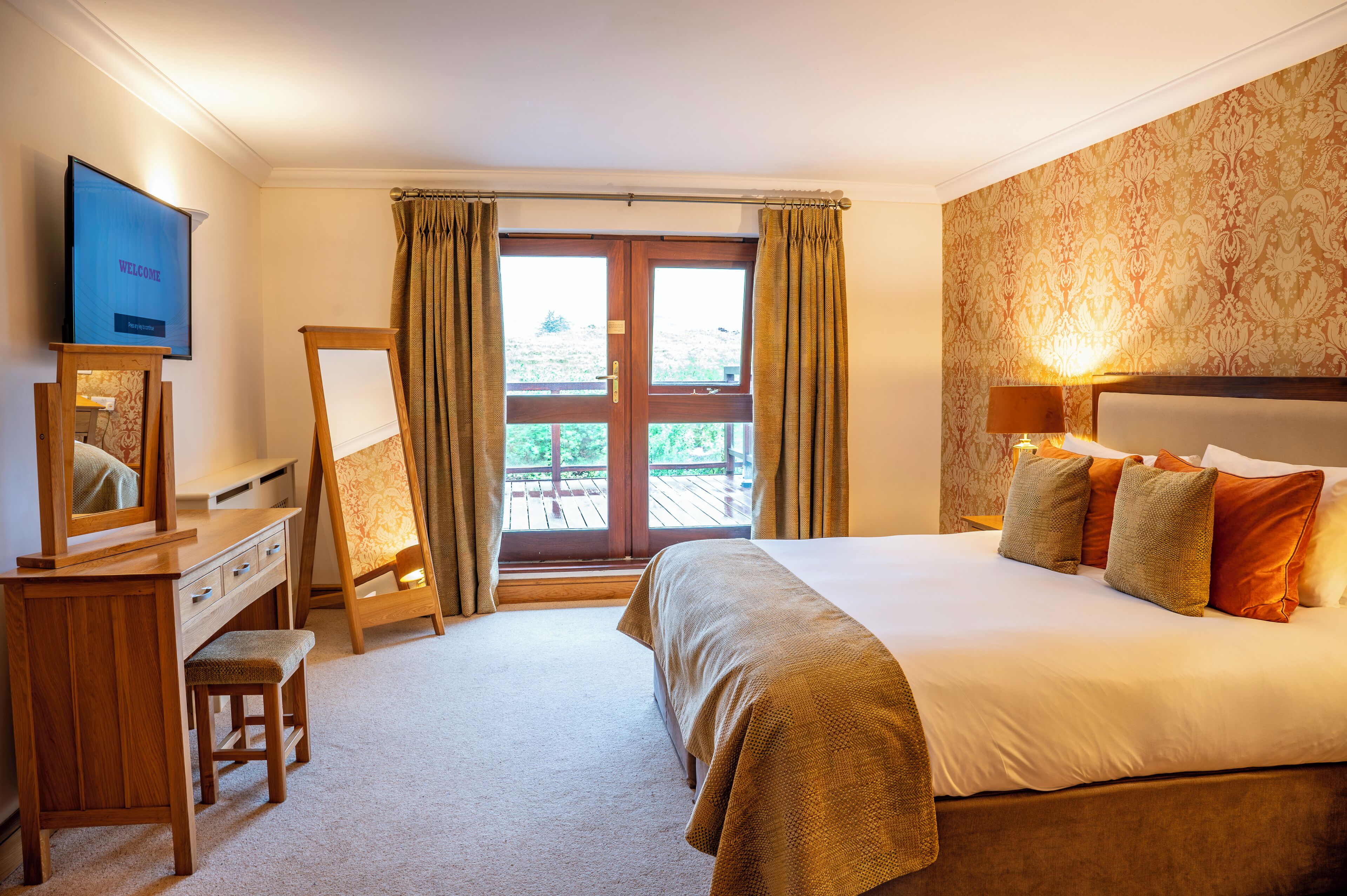 A hotel room with a bed, a desk, a television, a window with curtains, and a view of the outdoors.