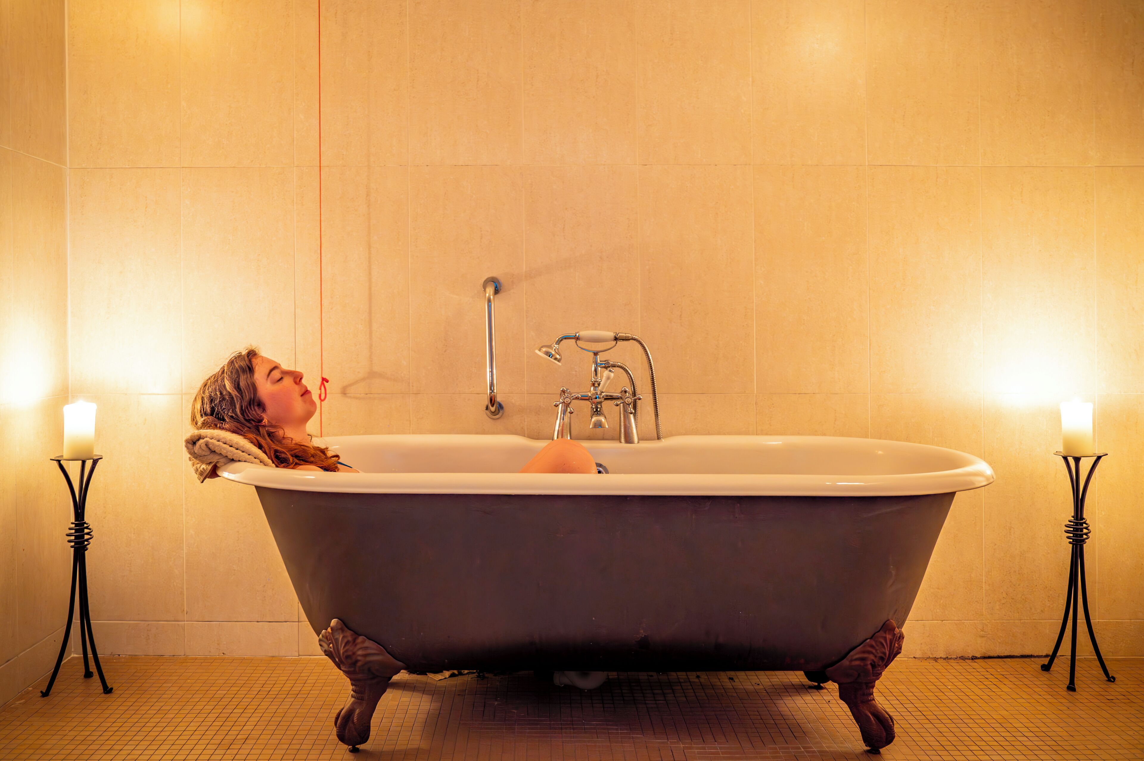 A bathtub with a towel, two candles, and a metal stand.