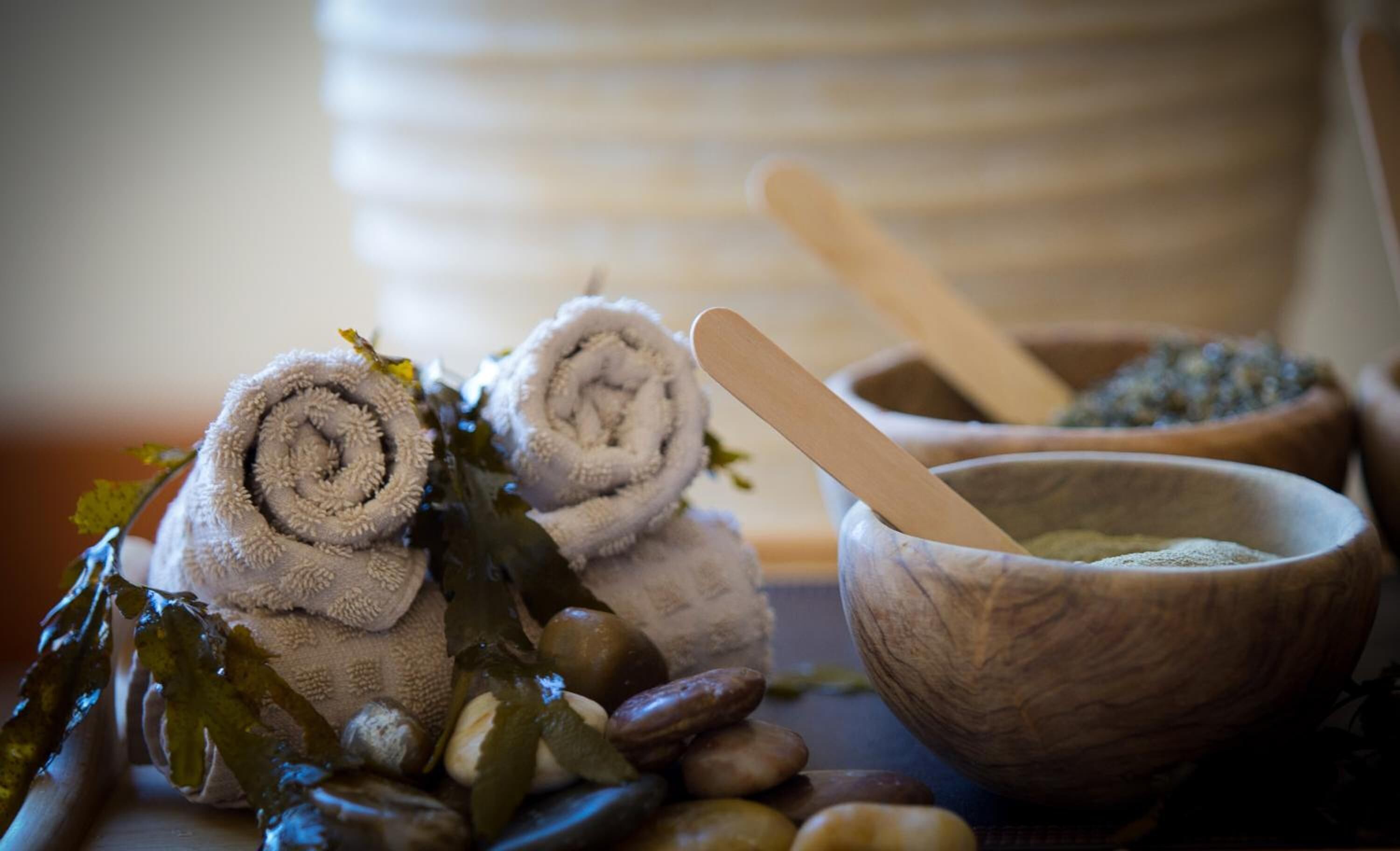 Un décor de spa avec des serviettes enroulées, une cuillère en bois dans un bol et quelques pierres.
