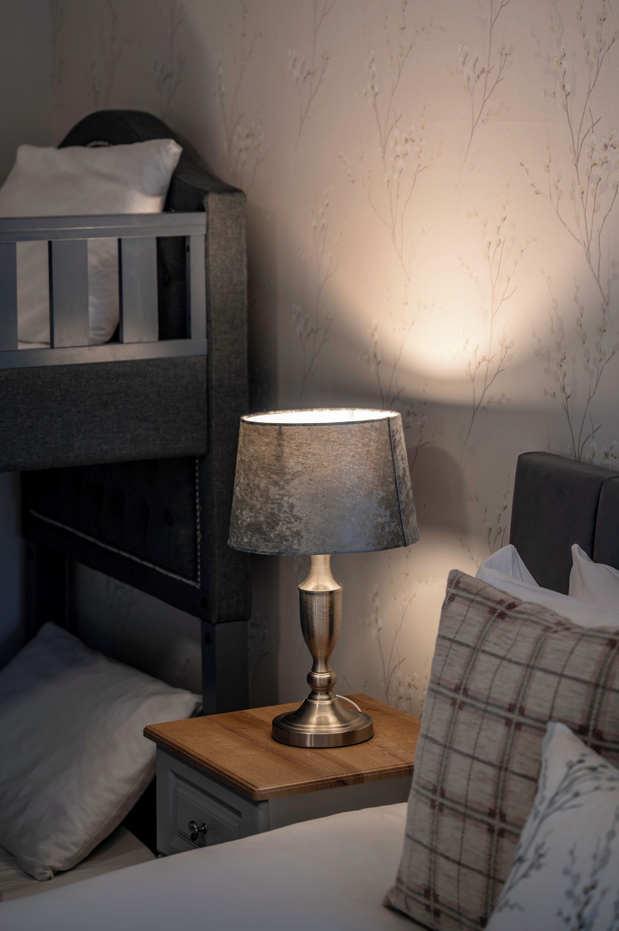 A bunk bed with a bedside table and lamp, a nightstand with a drawer, and a pillow on the bed.