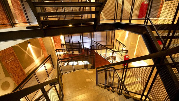 Una escalera interior de varios niveles con barandales de metal y piso de madera.