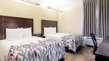 Una habitación de hotel con dos camas, un escritorio, un equipo de aire acondicionado y una ventana con cortinas.