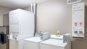 A laundry area with stacked washers and dryers, a coin-operated dryer, and a sign listing available detergents. - Red Roof Inn Locust Grove (Locust Grove)