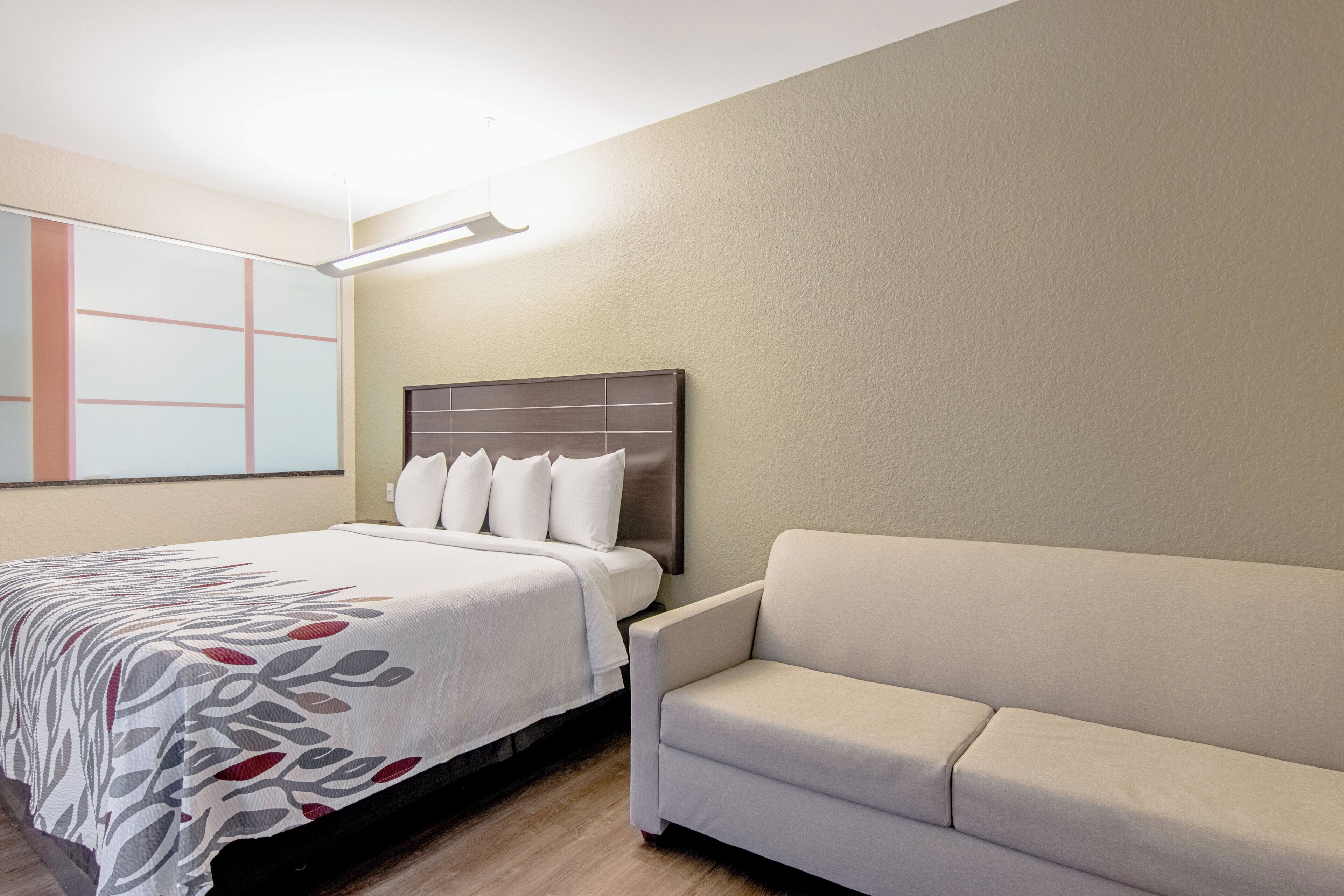 A hotel room with a bed, a headboard, a sofa, and a wall with a geometric design.