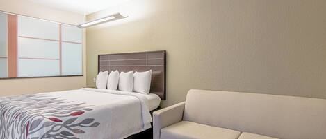 A hotel room with a bed, a headboard, a sofa, and a wall with a geometric design.