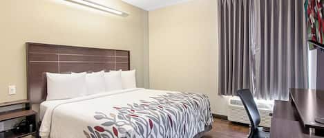 A hotel room with a large bed, a desk, a chair, and a window with curtains.