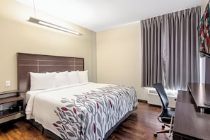 Una habitación de hotel con una cama grande, un escritorio, una silla y un ventanal con cortinas.