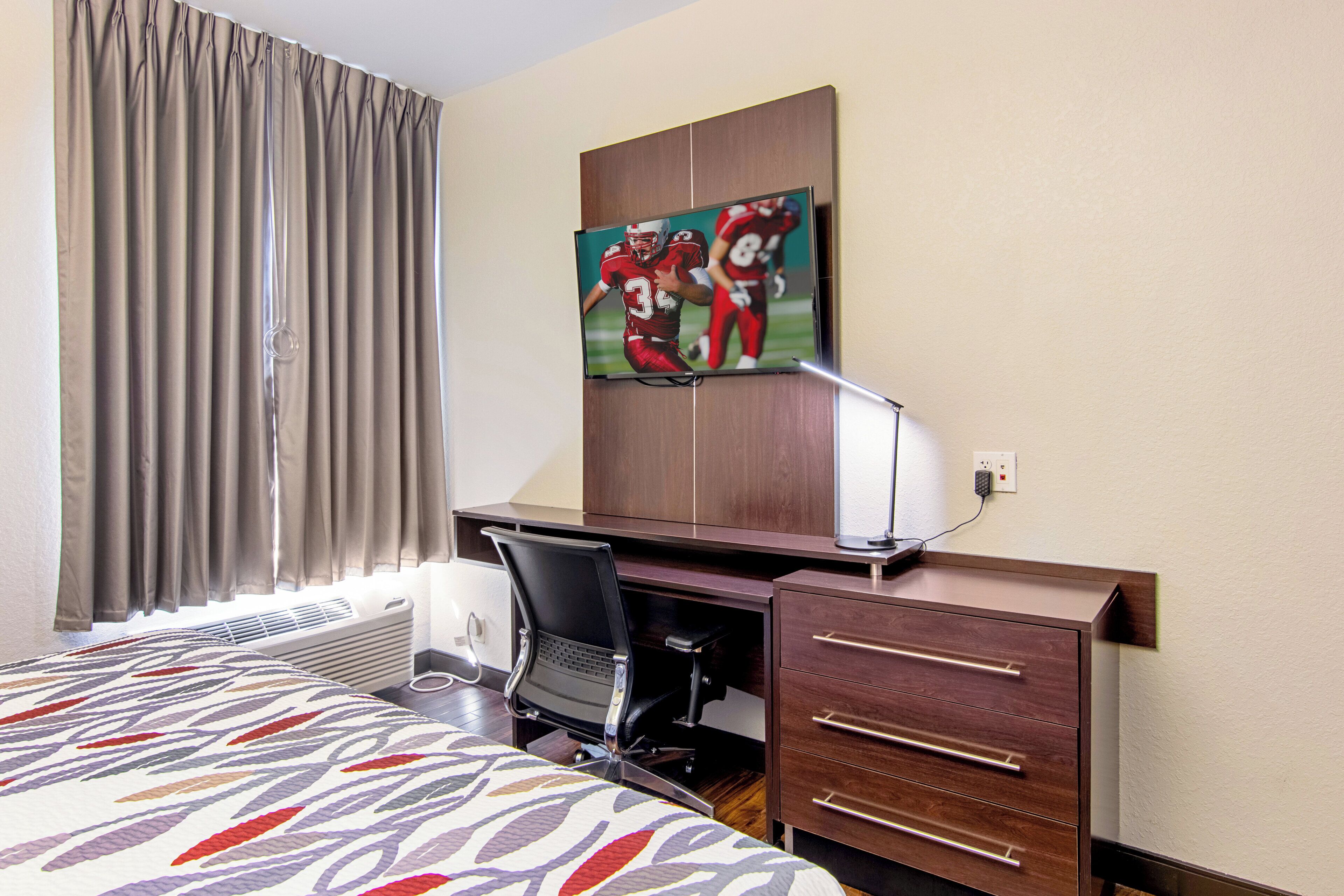 A hotel room with a bed, a desk, a chair, a dresser, and a painting on the wall.