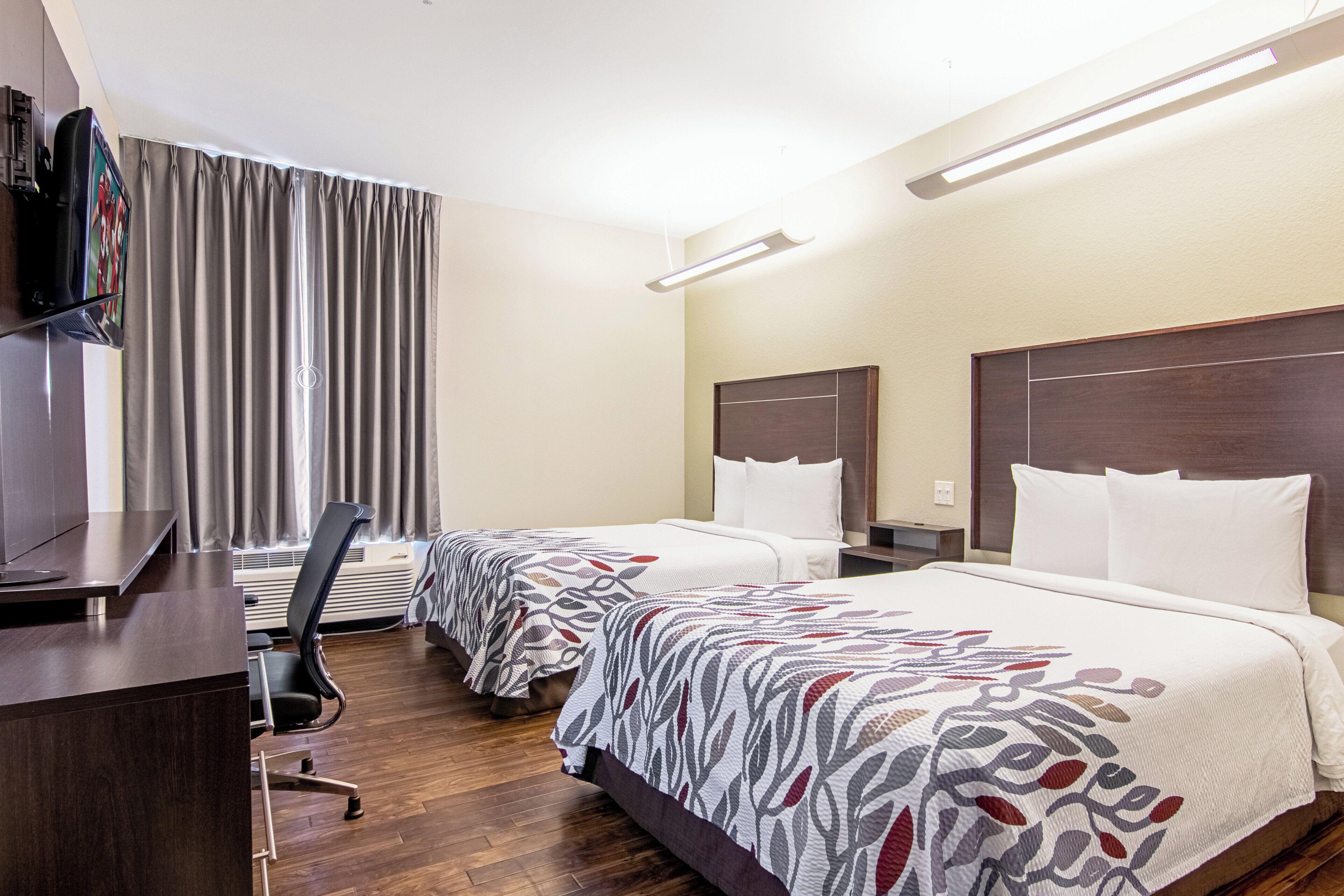 A hotel room with two beds, a desk, a television, and a chair.