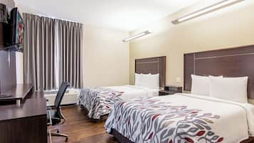 Ein Hotelzimmer mit zwei Betten, einem Schreibtisch, einem Fernseher und einem Sessel.