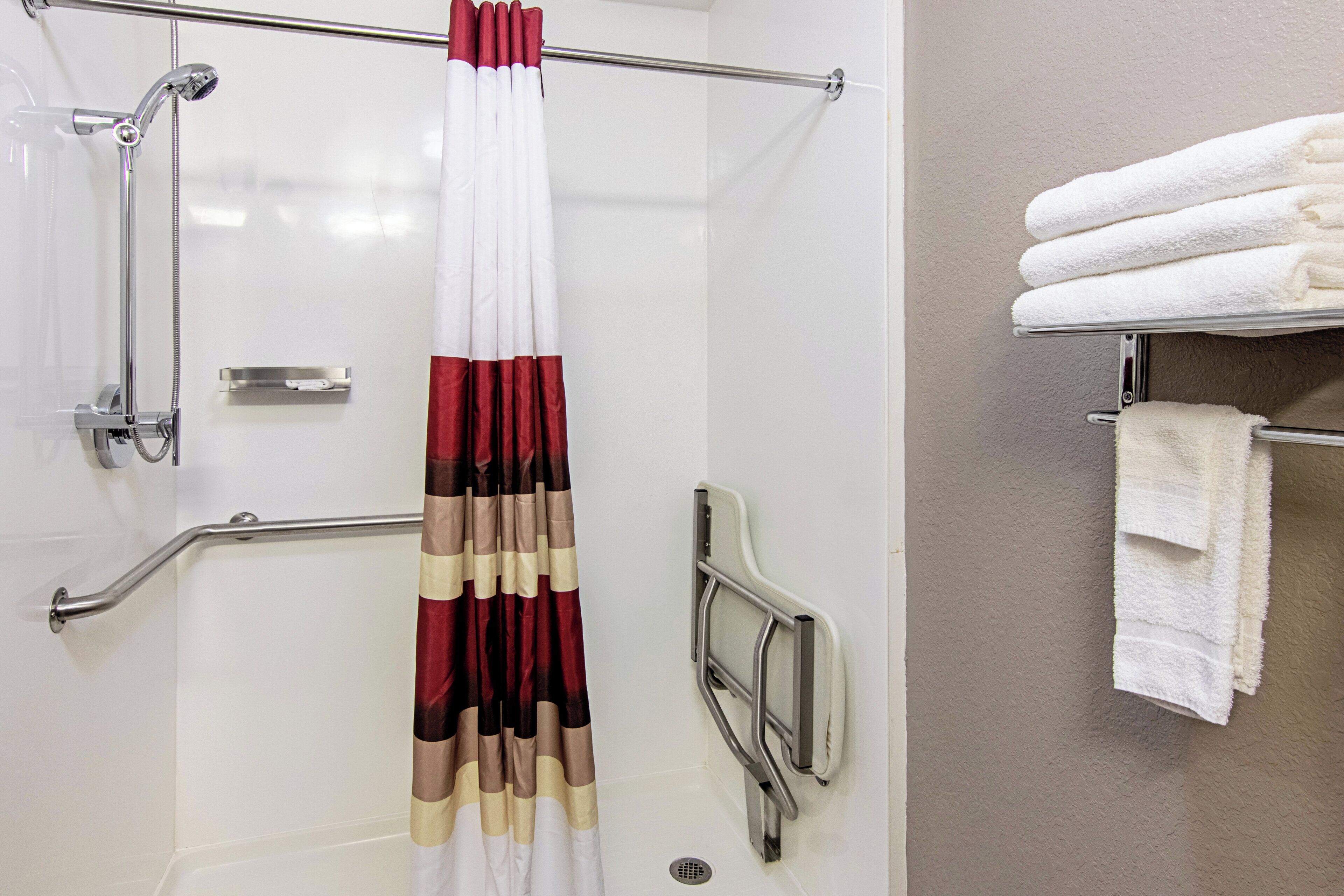A shower area with a handrail, a showerhead, and a towel rack with folded towels.
