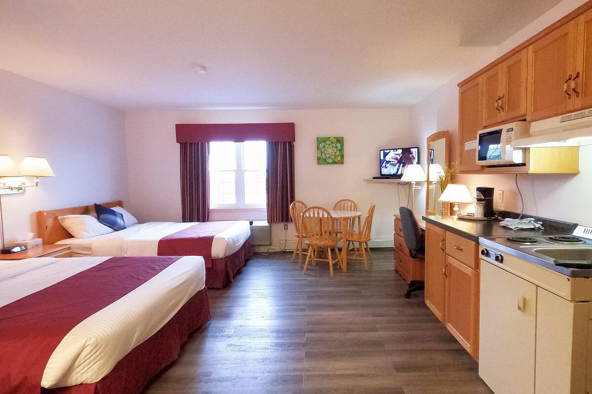 A hotel room with two beds, a dining table with chairs, a kitchen area with a microwave, and a television.