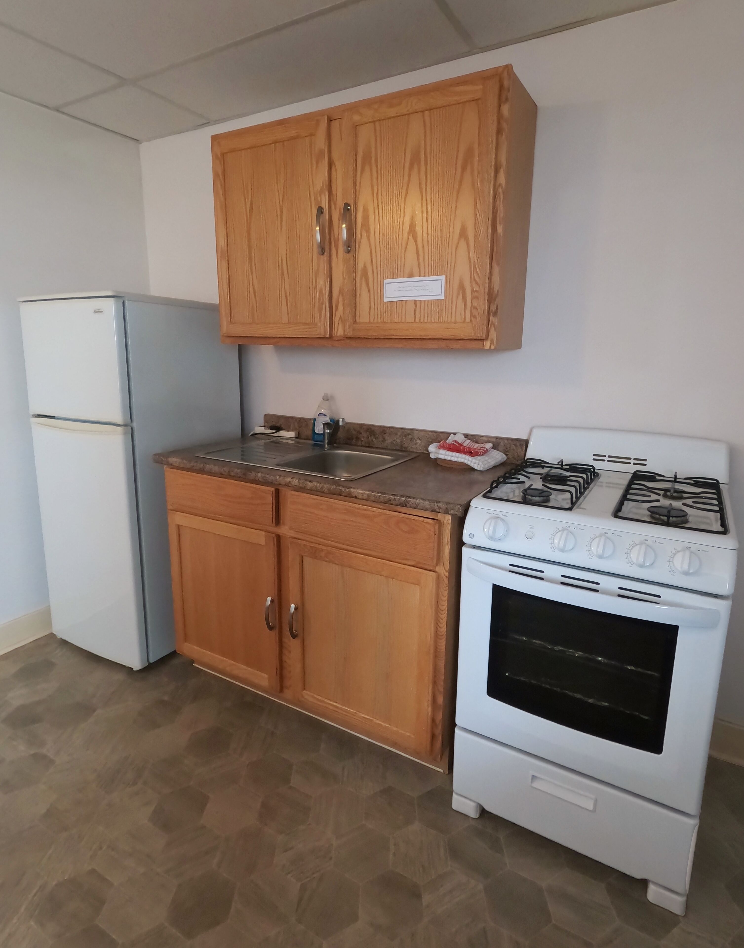 A kitchen with wooden cabinets, a refrigerator, a stove, and a sink.