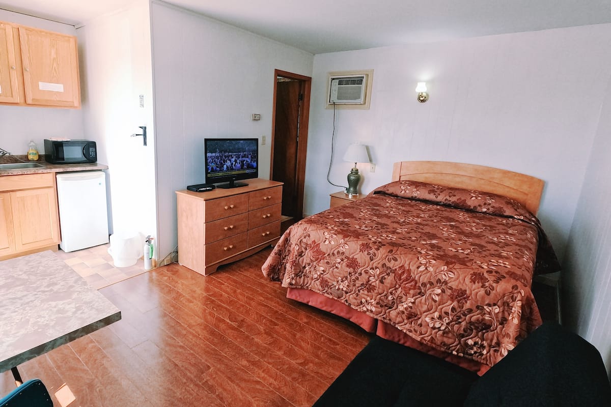 A bedroom with a bed, a TV on a dresser, a microwave, and a small refrigerator.