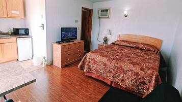 Une chambre avec un lit, un téléviseur posé sur une commode, un four à micro-ondes et un petit réfrigérateur.