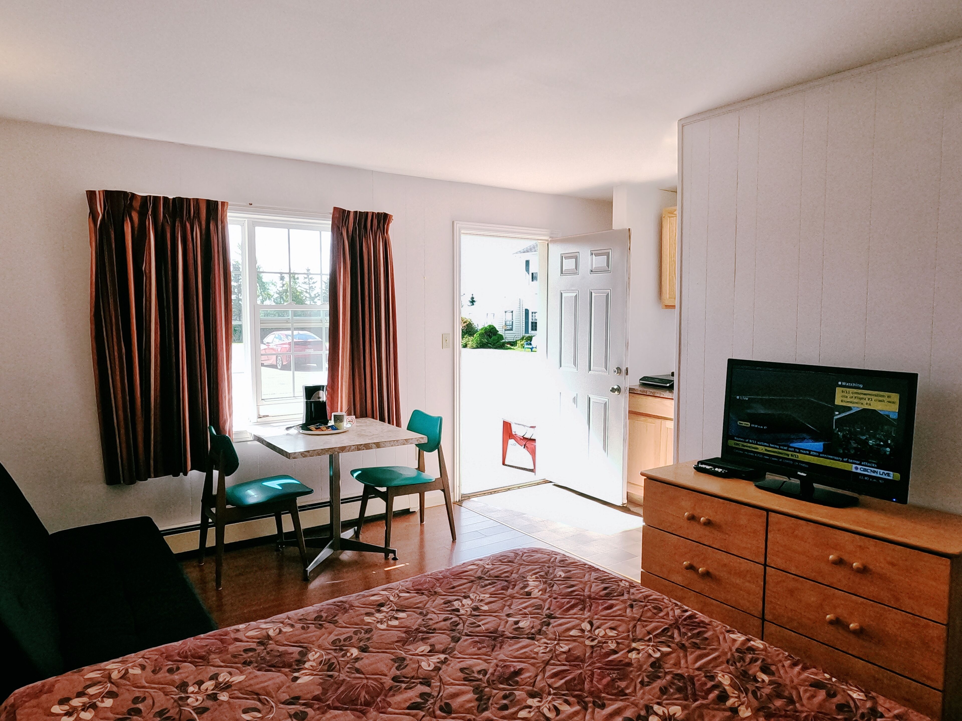 A room with a bed, a desk, a chair, a television, and a door leading outside.