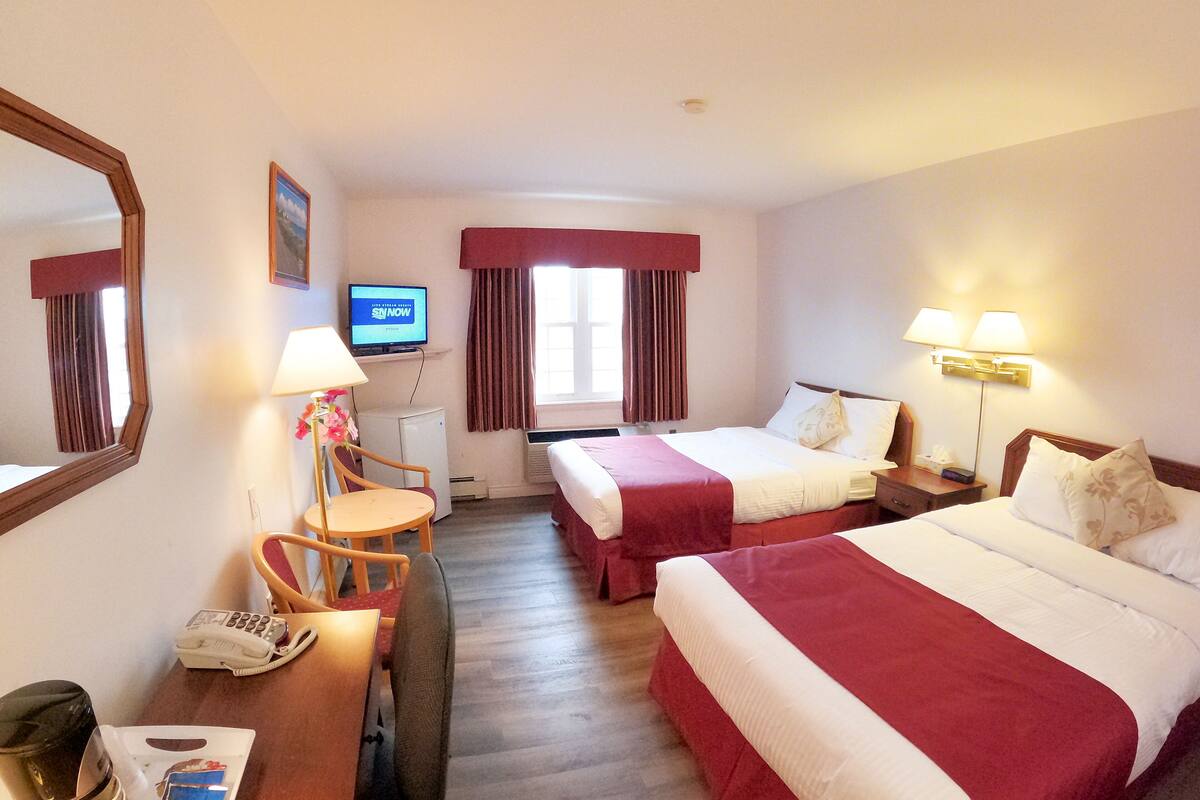 A hotel room with two beds, a desk with a chair, a television, and a window with curtains.