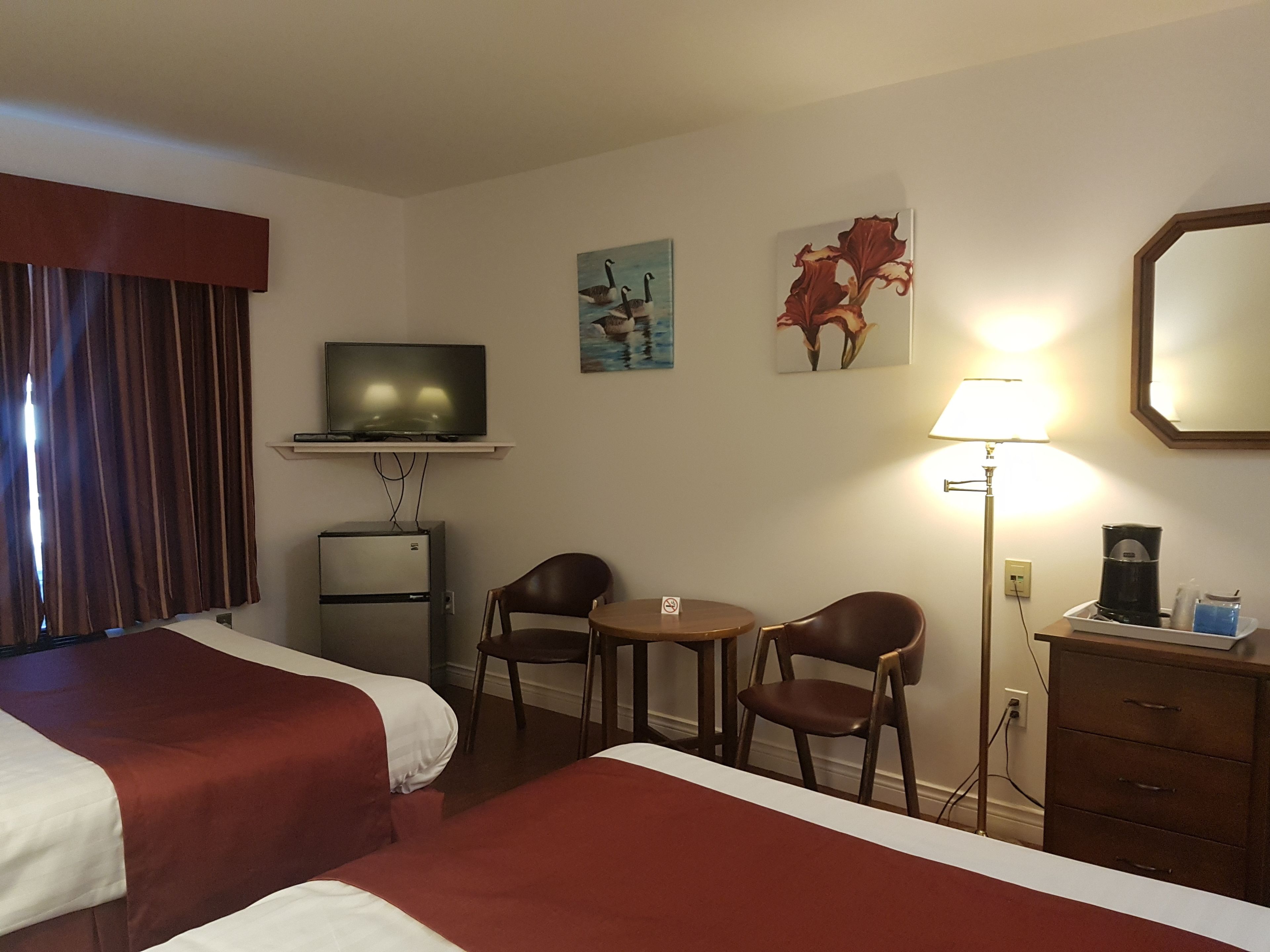 A hotel room with two beds, a television, a desk with two chairs, a coffee maker, and artwork on the walls.