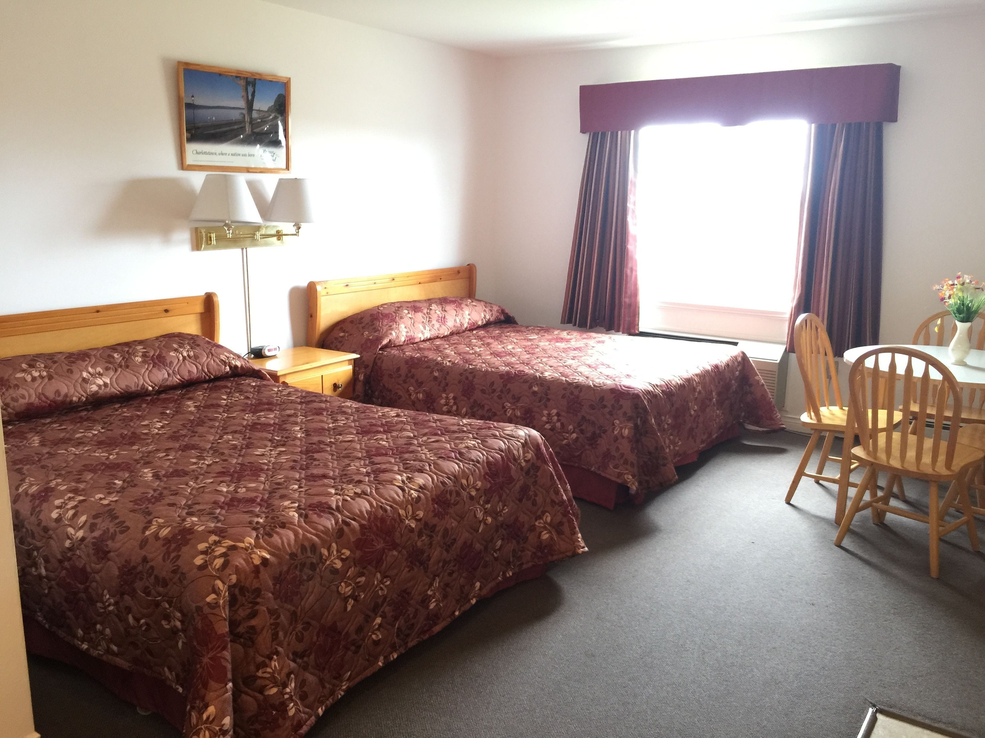 Ein Hotelzimmer mit zwei Betten, einem Schreibtisch, einem Stuhl, einer Lampe und einem Fenster mit Vorhängen.