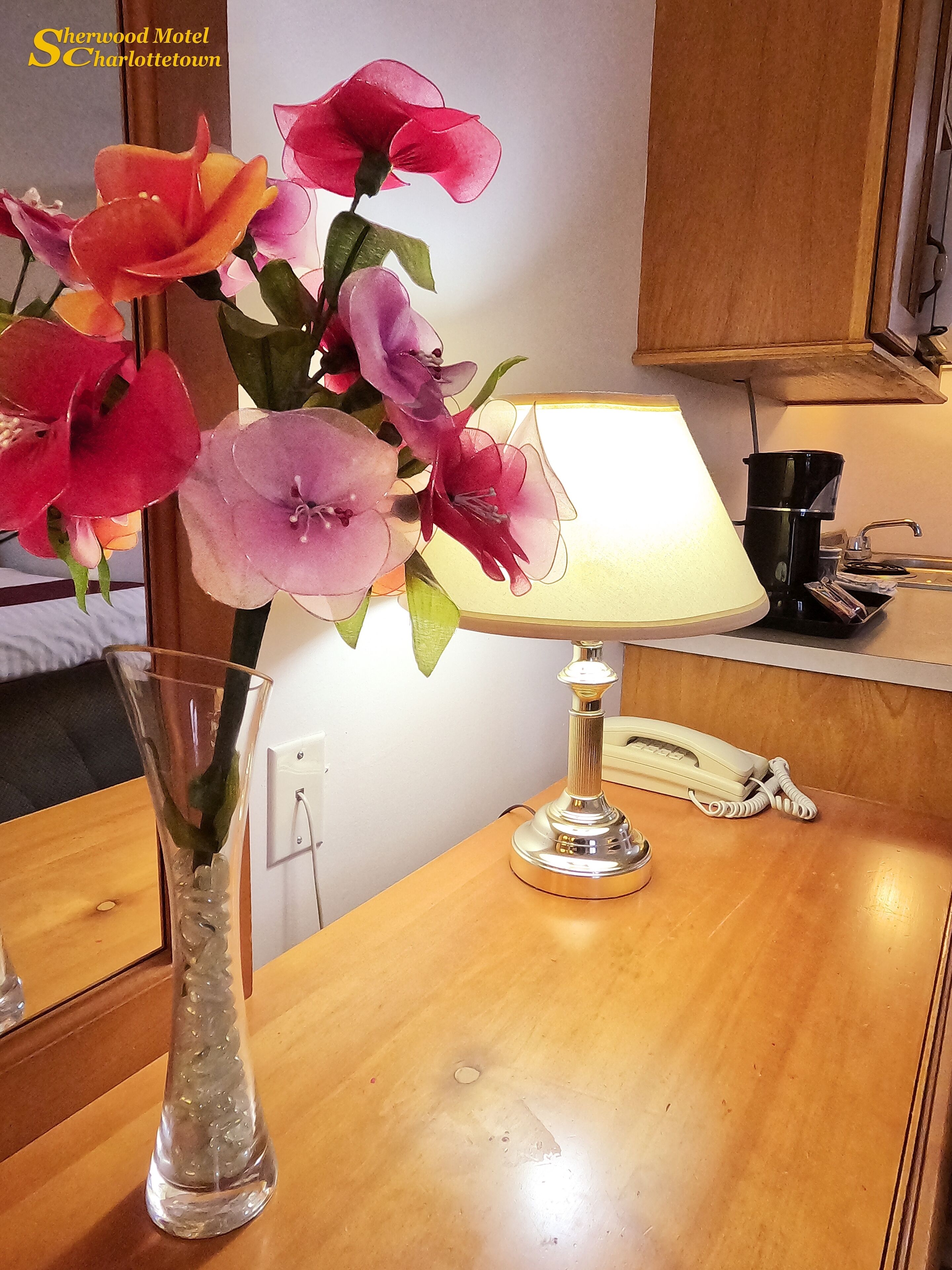 Een houten tafel met een lamp, een telefoon en een vaas met bloemen.