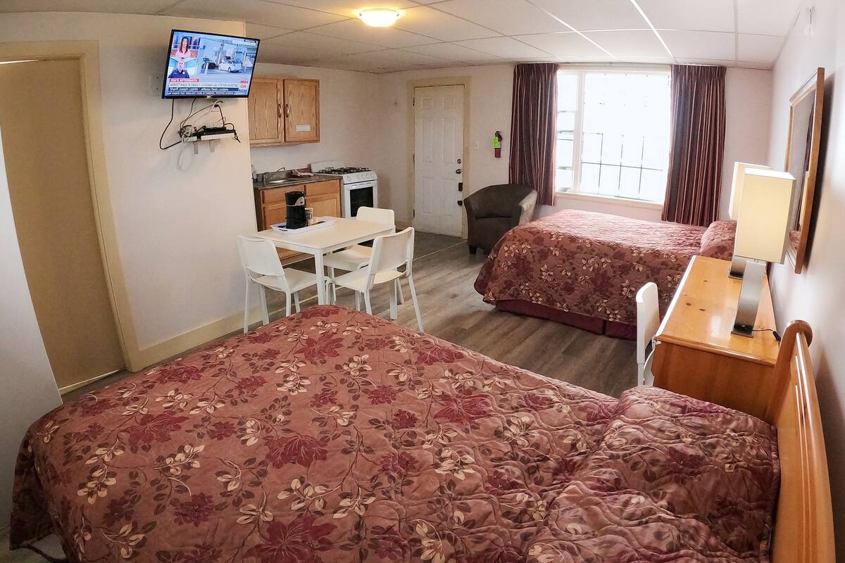 A hotel room with two beds, a desk, a chair, a television, and a window with curtains.