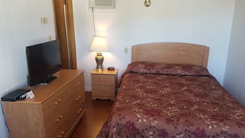 A bedroom with a bed, a dresser, a TV, a lamp, and a wall-mounted air conditioner.