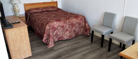 A bedroom with a bed, a desk, a chair, and a lamp.