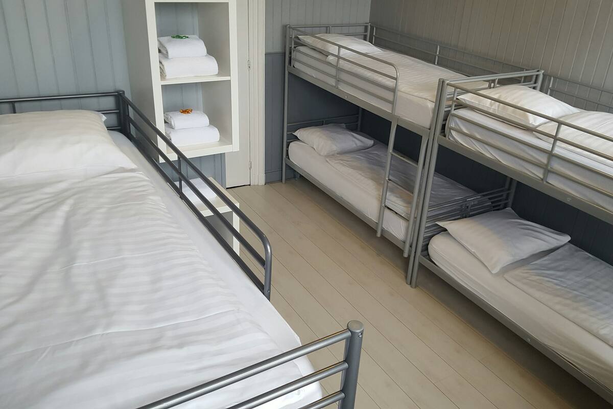 Une chambre avec un lit superposé, deux lits, une étagère avec des serviettes pliées et un plancher en bois.
