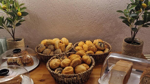 A table with baskets of bread and pastries, a plate with a sandwich, and two potted plants.