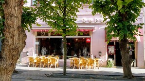 A café with outdoor seating, a pink awning, and a visible storefront.