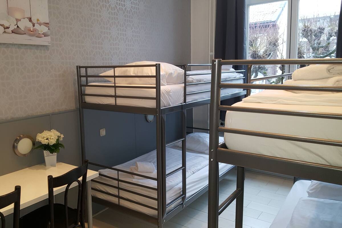 Une chambre avec un lit superposé, un bureau et une chaise, un vase avec des fleurs et une fenêtre donnant sur un beau paysage.