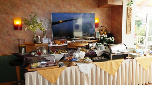 A buffet setup with various food items, a television, and decorative elements like flowers and wall sconces.