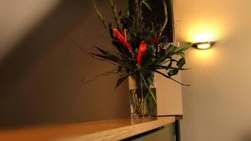 A vase with flowers on a wooden surface near a wall with a light fixture.