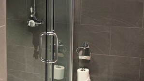 A shower with a glass door, a toilet paper holder, and a towel rack. - The Penny Farthing (Berkhamsted)