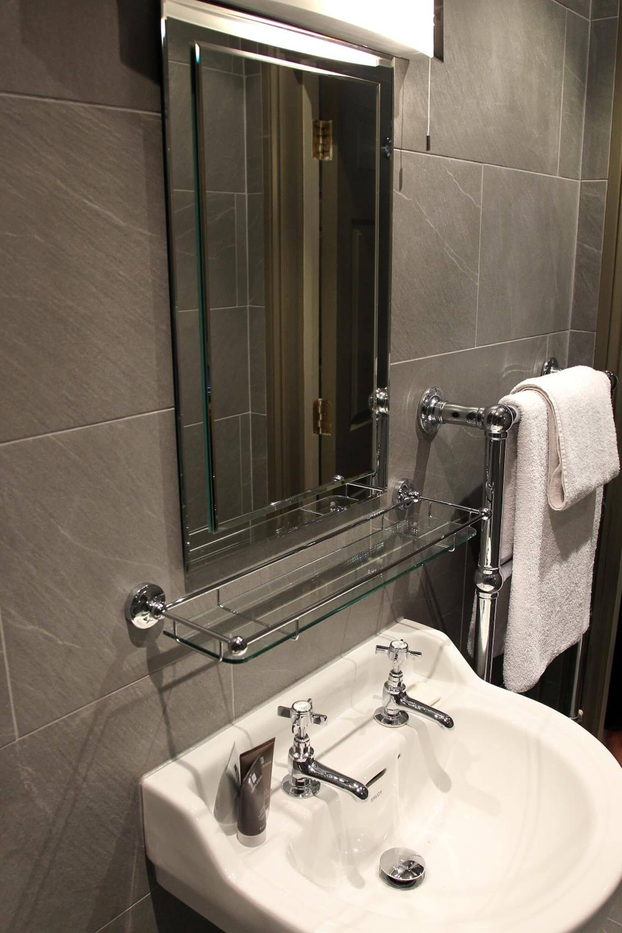 Ein Badezimmer mit einer Duschkabine aus Glas, einem weißen Waschbecken mit Chromarmaturen und einem Handtuchhalter mit einem weißen Handtuch.