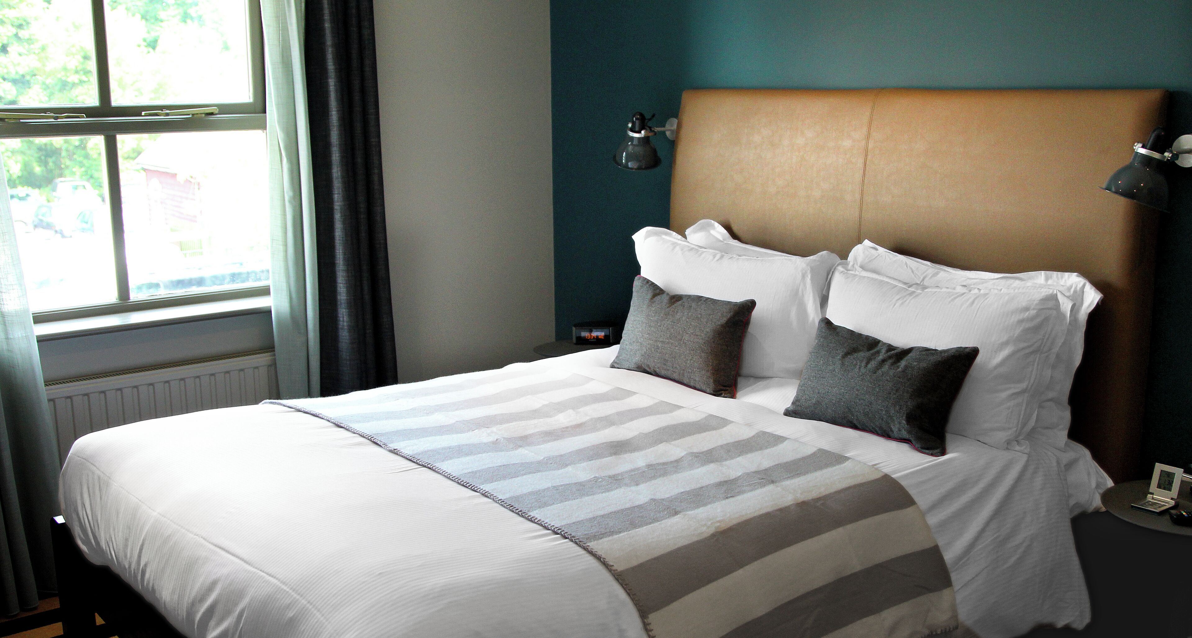 A neatly made bed with a striped bedspread, a headboard, and a bedside lamp.