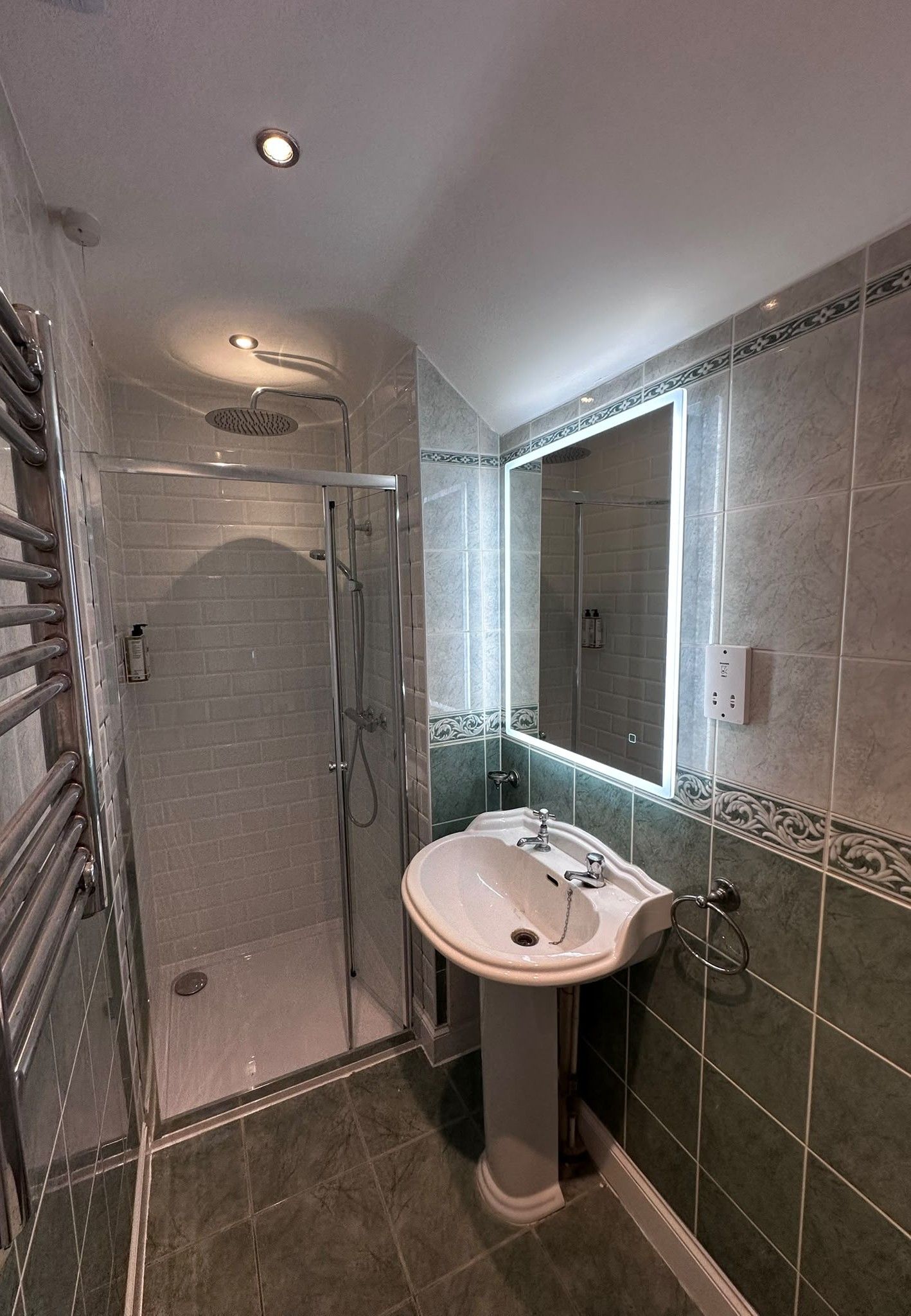 Een badkamer met een douchecabine van glas, een wastafel op een voetstuk en een spiegel met een decoratieve lijst.